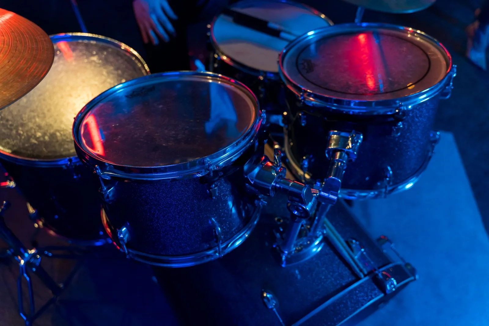 Vibrant close-up of a drum set with blue and red stage lighting creating a lively atmosphere.
