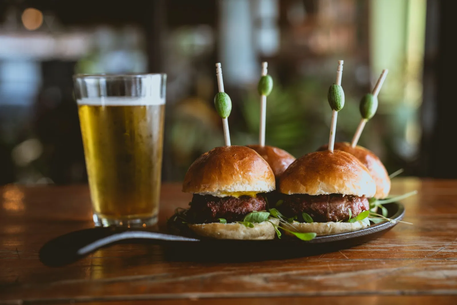 Close-up of gourmet sliders with olives and a beer glass on a wooden table, perfect for culinary and dining themes.