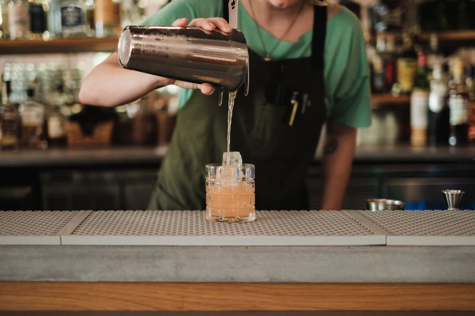 A bartender pours a cocktail into a glass at a stylish bar, showcasing expert preparation.