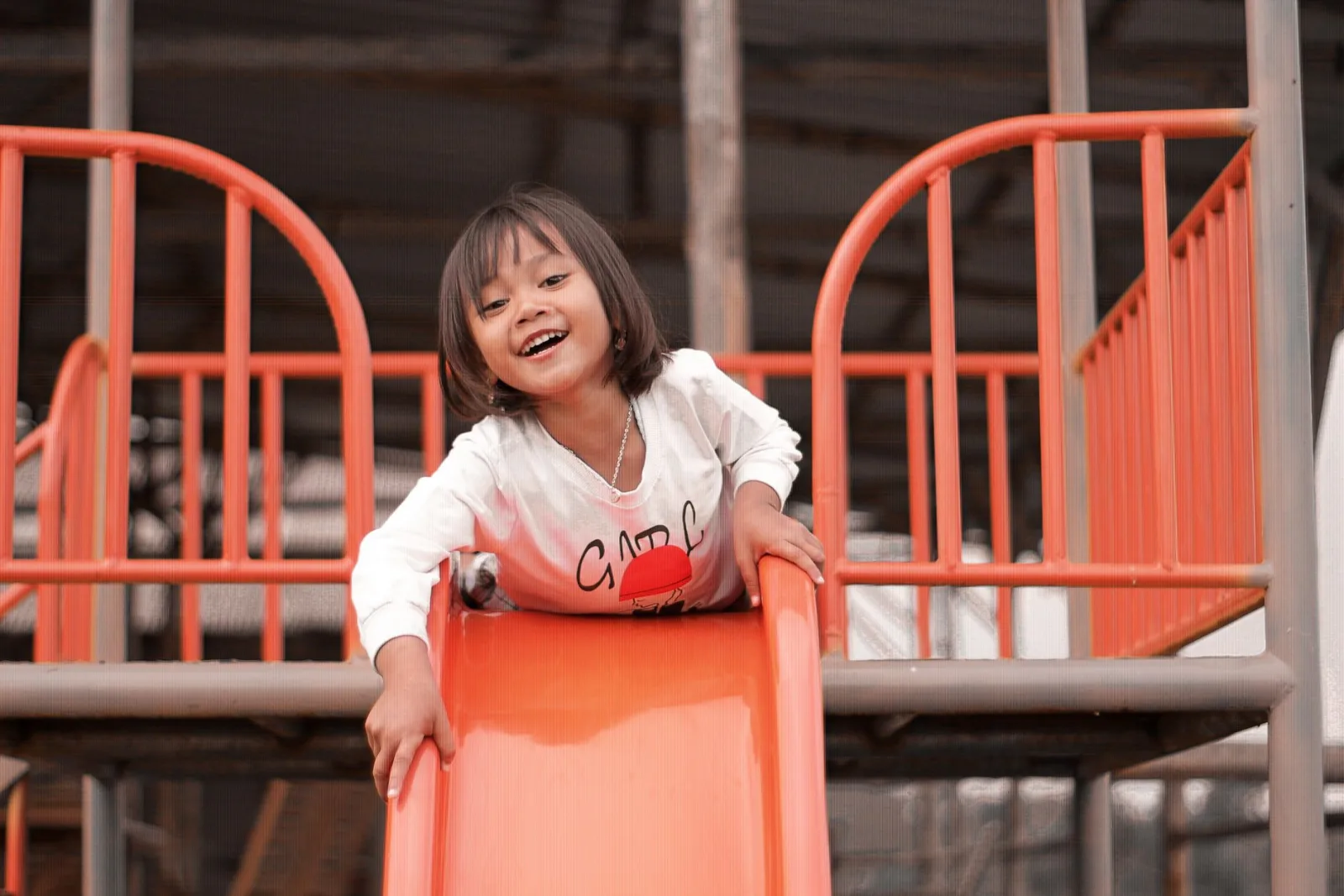 A happy child enjoying playtime on a vibrant orange slide at an outdoor playground.