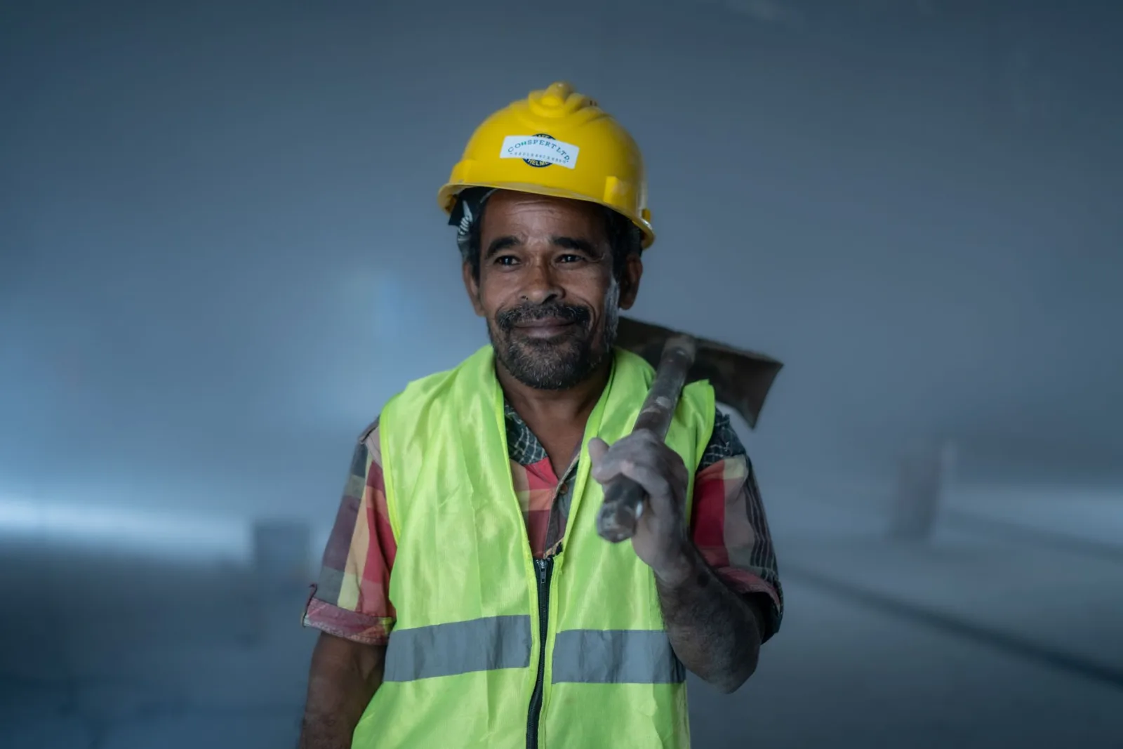 Smiling construction worker in safety gear holding a tool indoors. Professional and industrial theme.