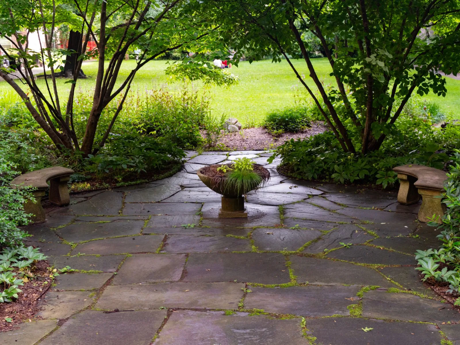 Peaceful stone patio surrounded by greenery and a central plant centerpiece in a New York garden.