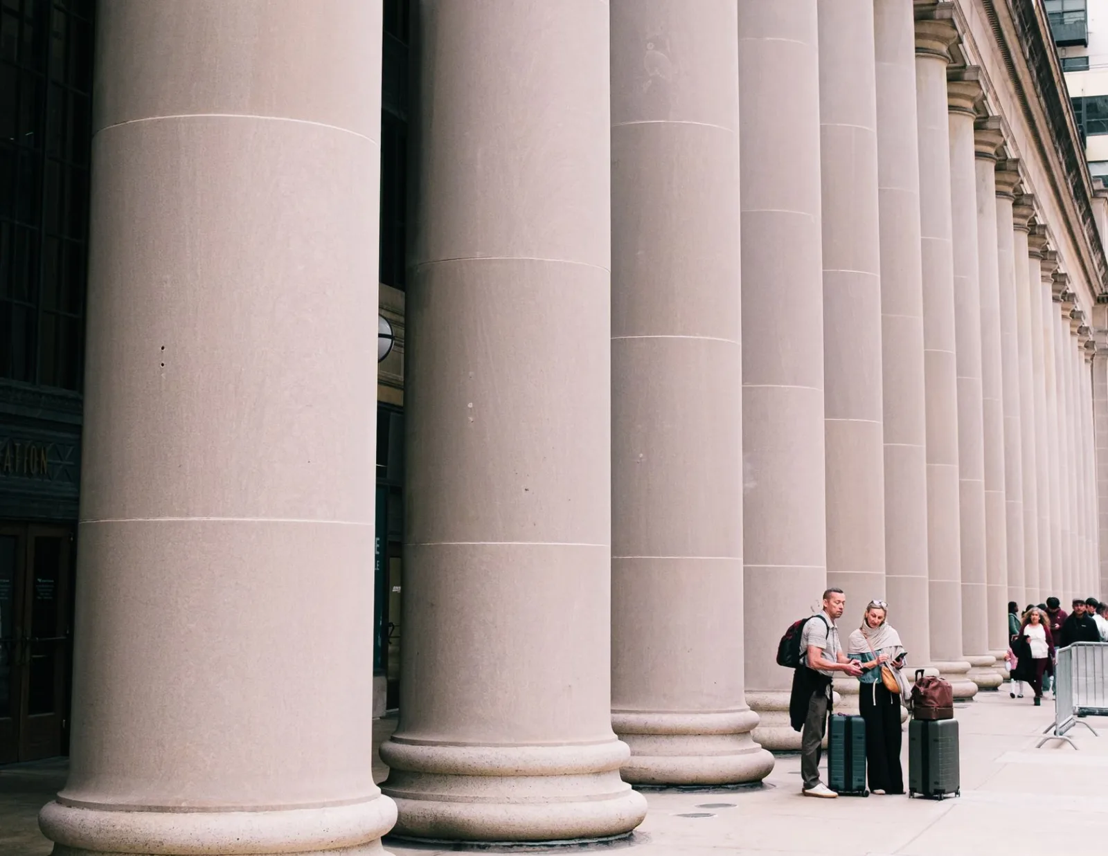 Two travelers stand beside large columns in Chicago, capturing the essence of urban exploration and architectural beauty.