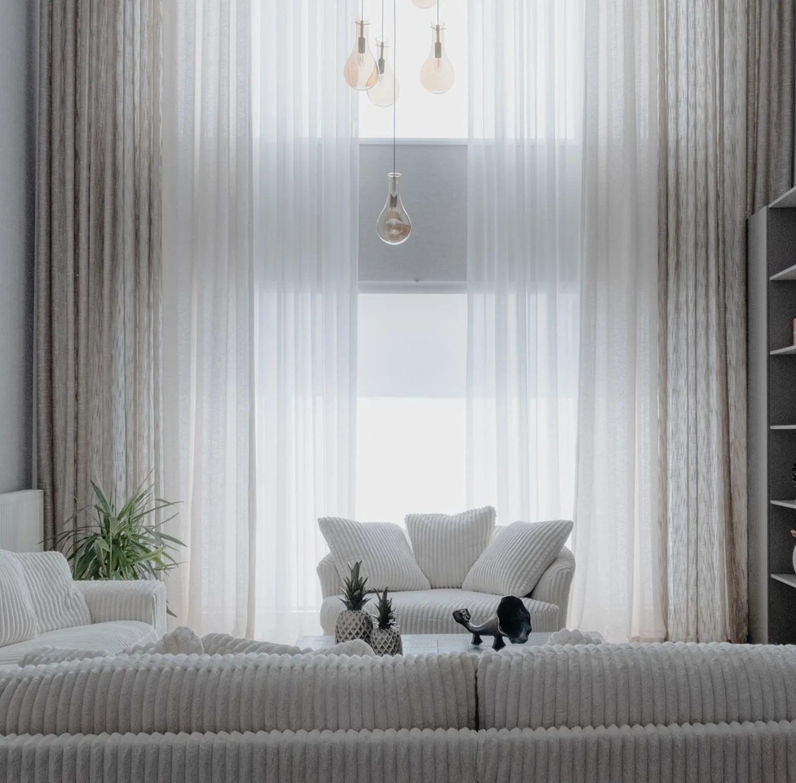 A minimalist living room with soft white sofas and large curtains, creating a cozy atmosphere.